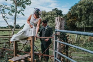 Alternative bride with purple hair and flower crown climbing over stye on wedding day